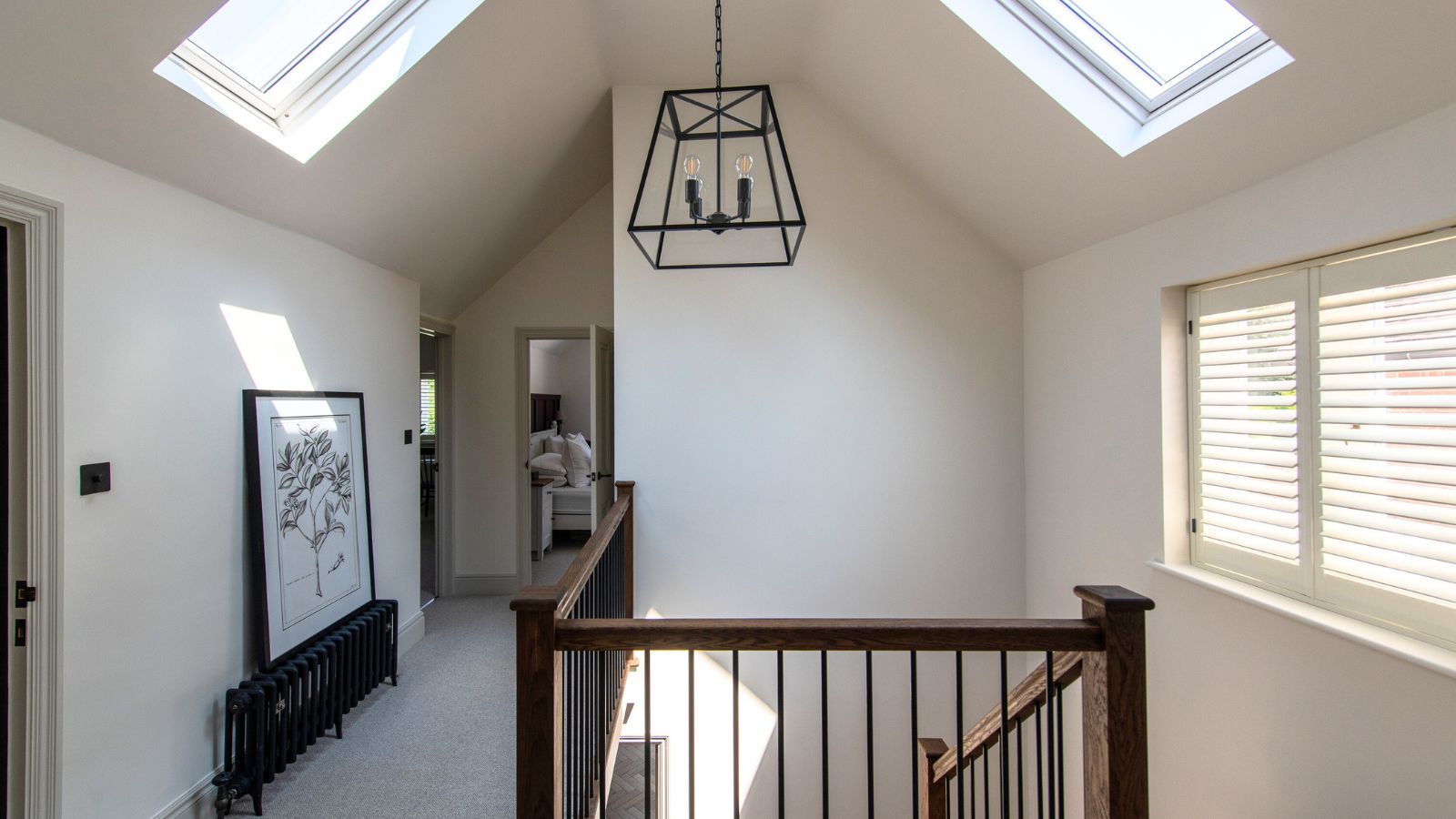 A bright, airy landing with skylights flooding the space with natural light. White walls and shutters reflect light beautifully, while a black-framed pendant and staircase add modern contrast.
