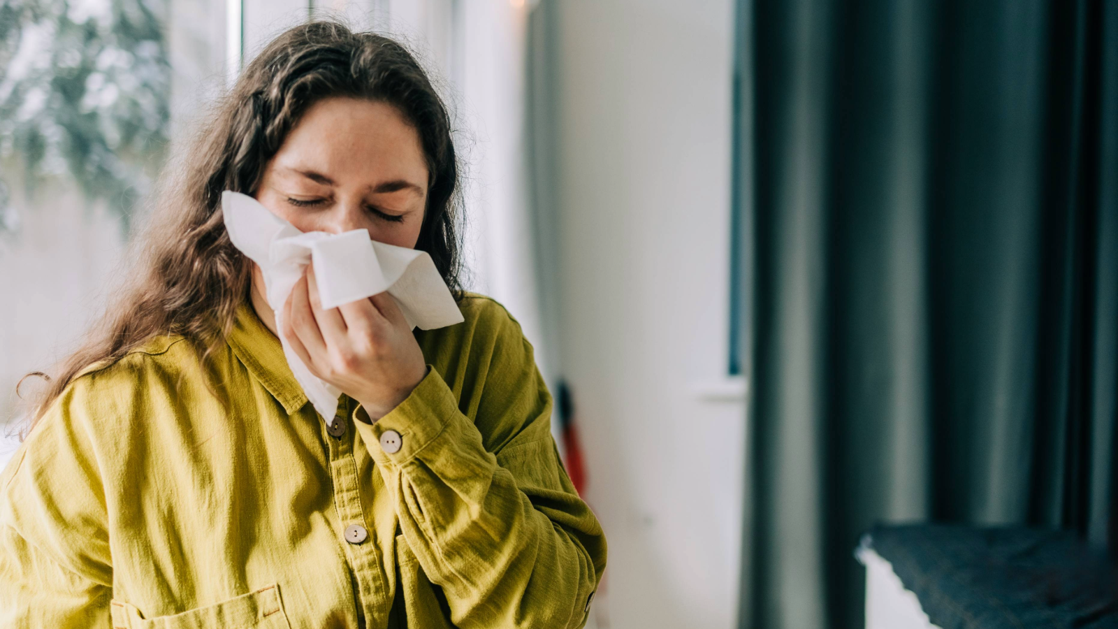 Woman wearing a yelllow shirt blowing her nose with a tissue