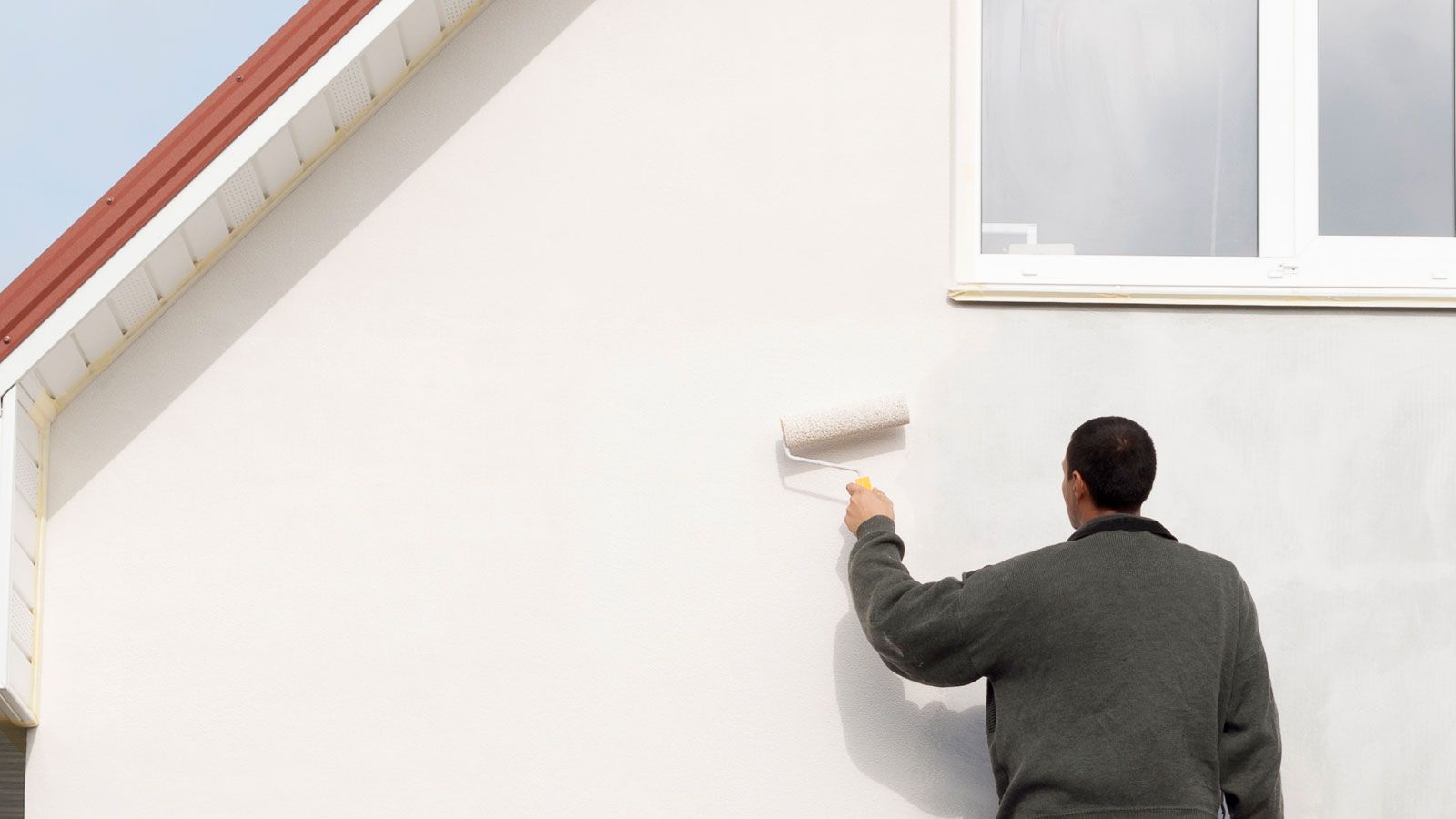 Man up a ladder painting the exterior of a house cream with a roller