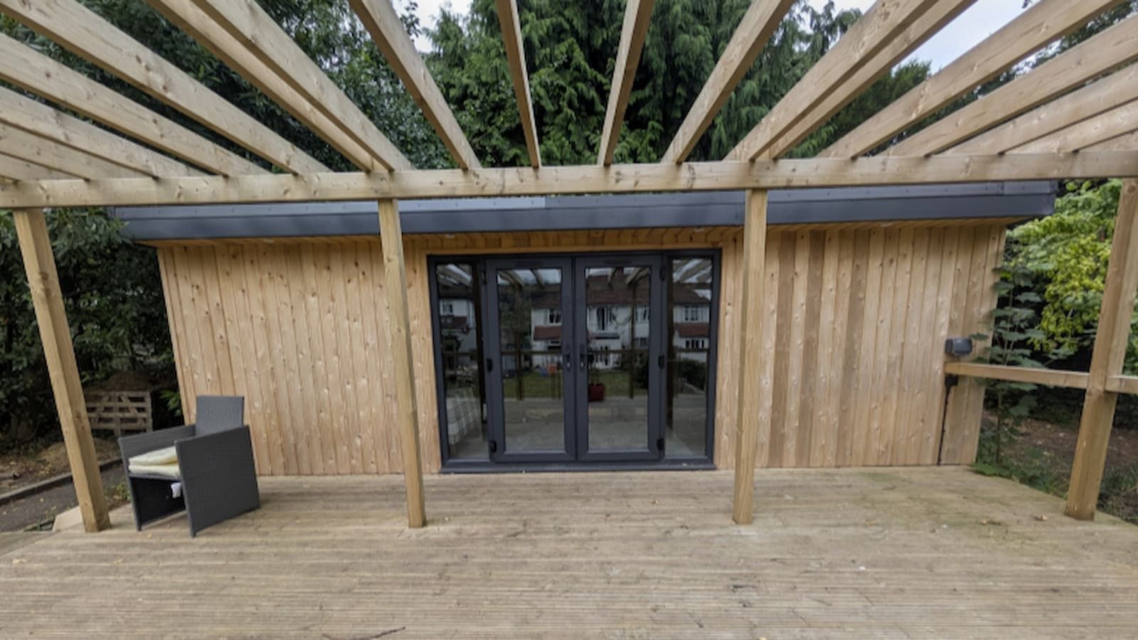 A wooden outbuilding with black doors and wooden patio