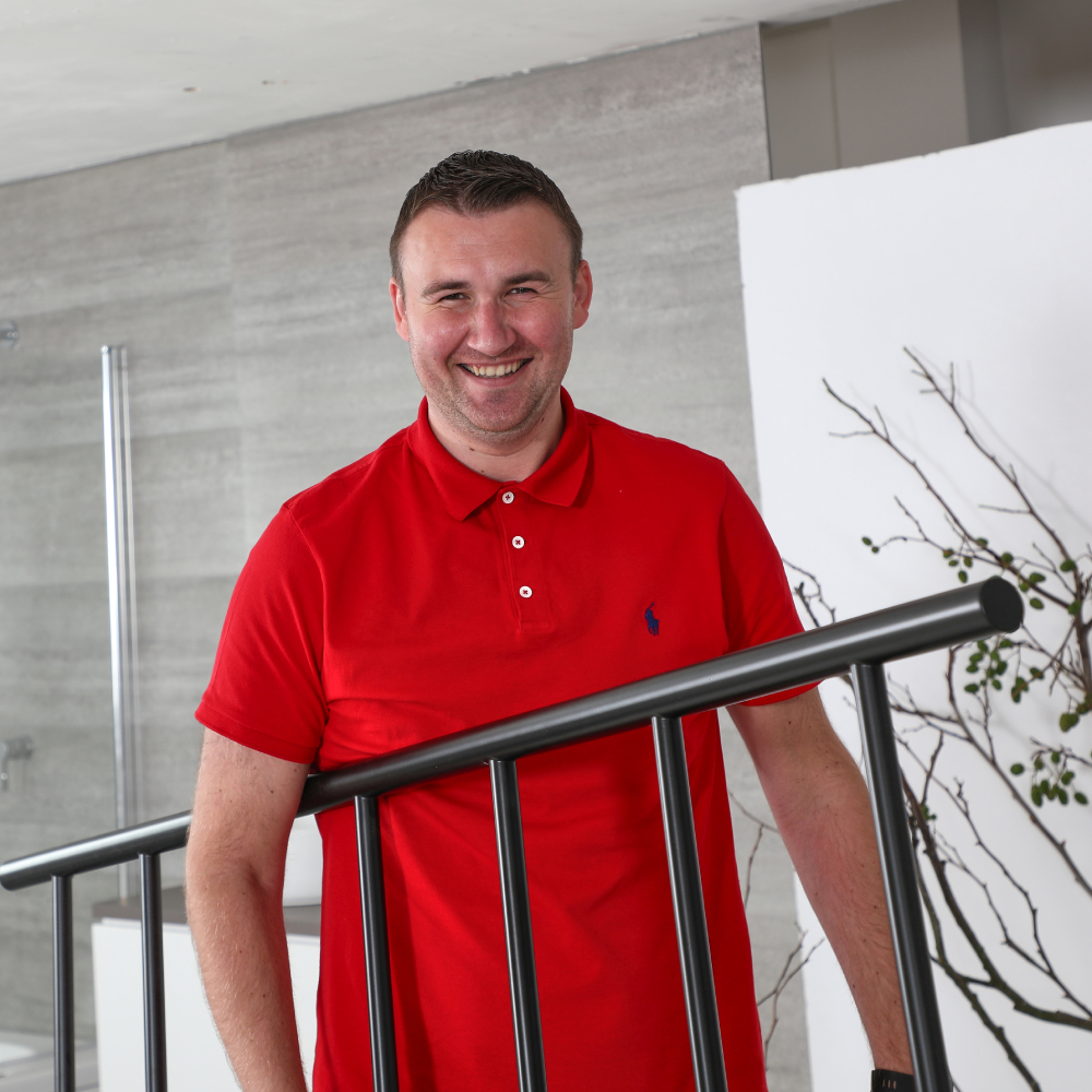 male in bathroom with short dark hair, wearing red polo shirt and carrying black towel ladder radiator
