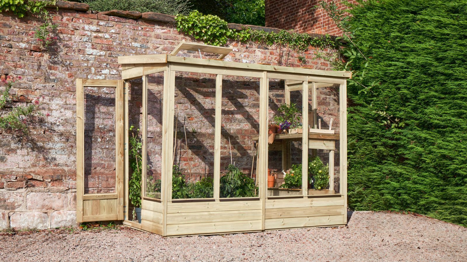 A wooden lean-to greenhouse set against a red brick garden wall