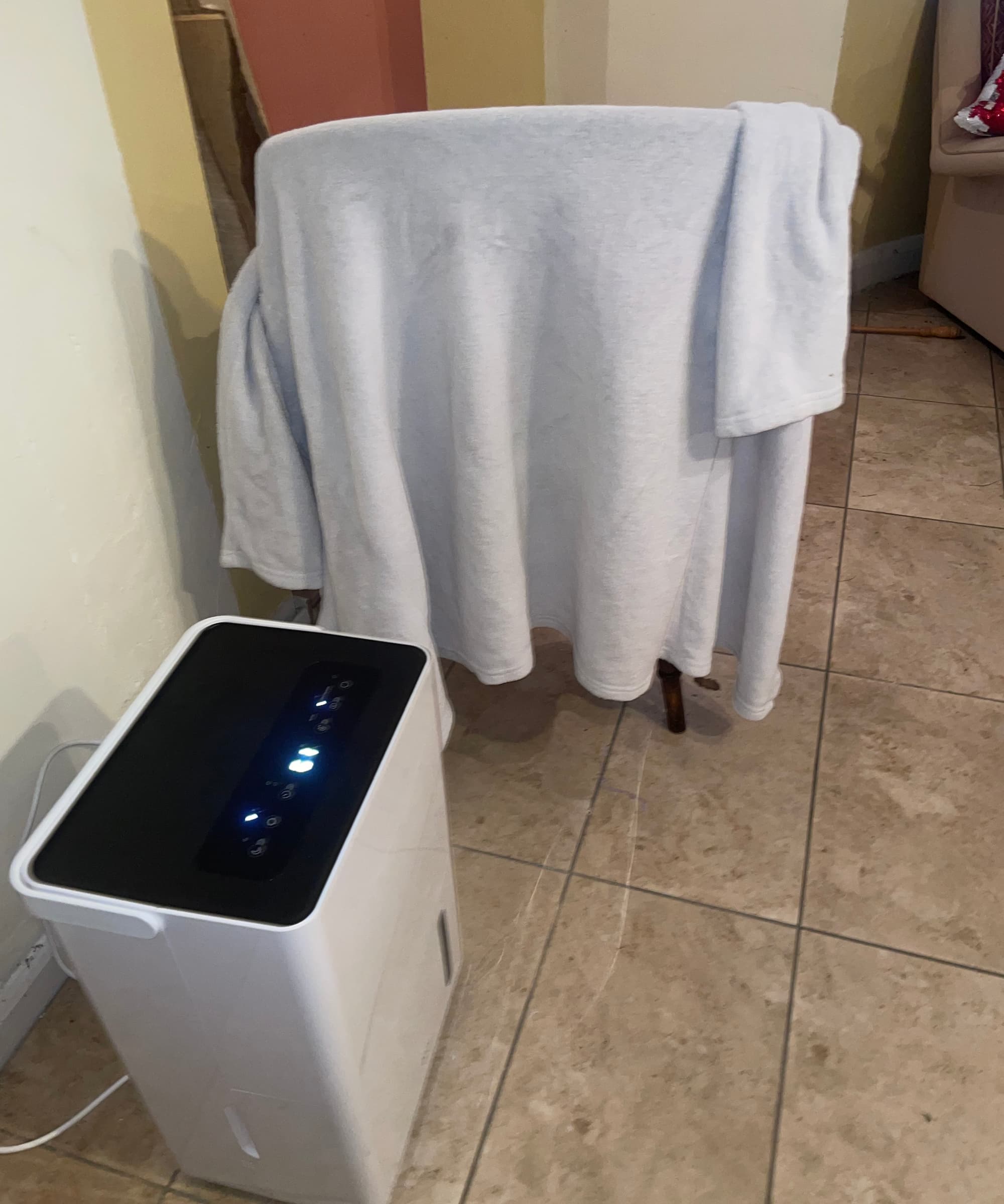 A Duux Bora Smart Dehumidifier drying out a robe on a chair