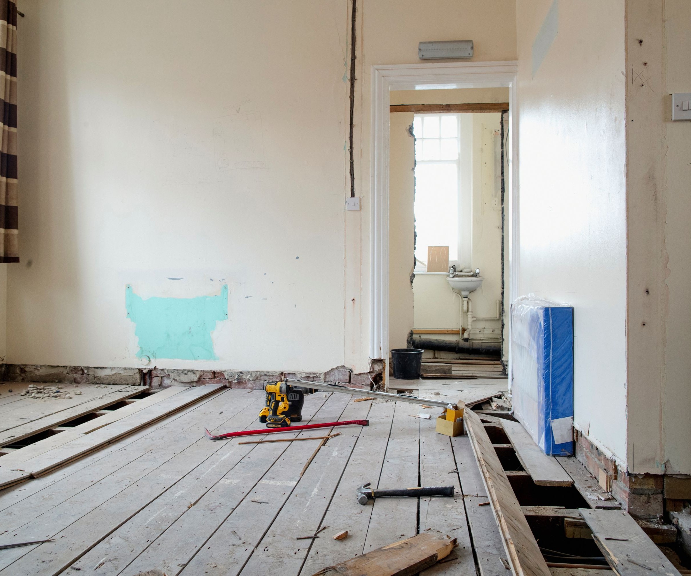 A bare room with a wooden floor and floorboards lifted up with tools in the centre of the room
