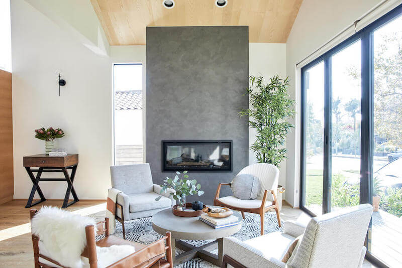 Bright living room centered on gray plaster fireplace, surrounded by modern seating, patterned rug, and full height windows to the street.
