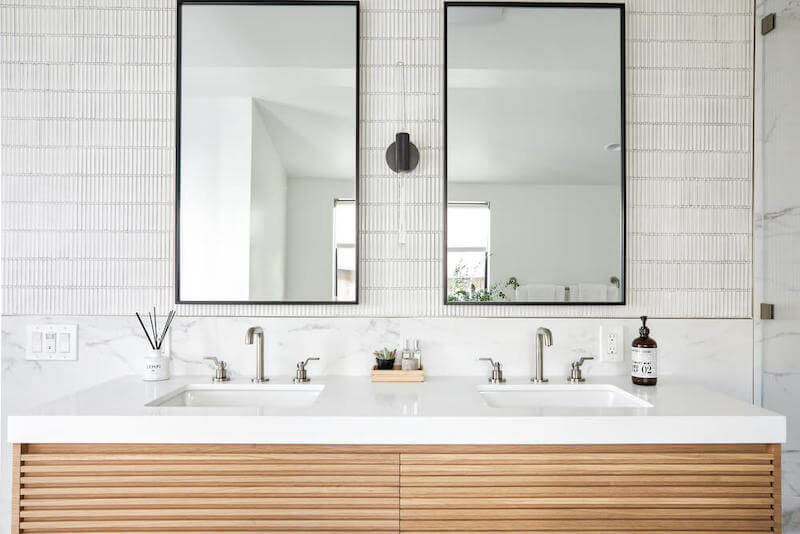 Modern bathroom with fluted wood double vanity, white quartz countertop, two undermount sinks, tall mirrors, and slim stacked wall tile.