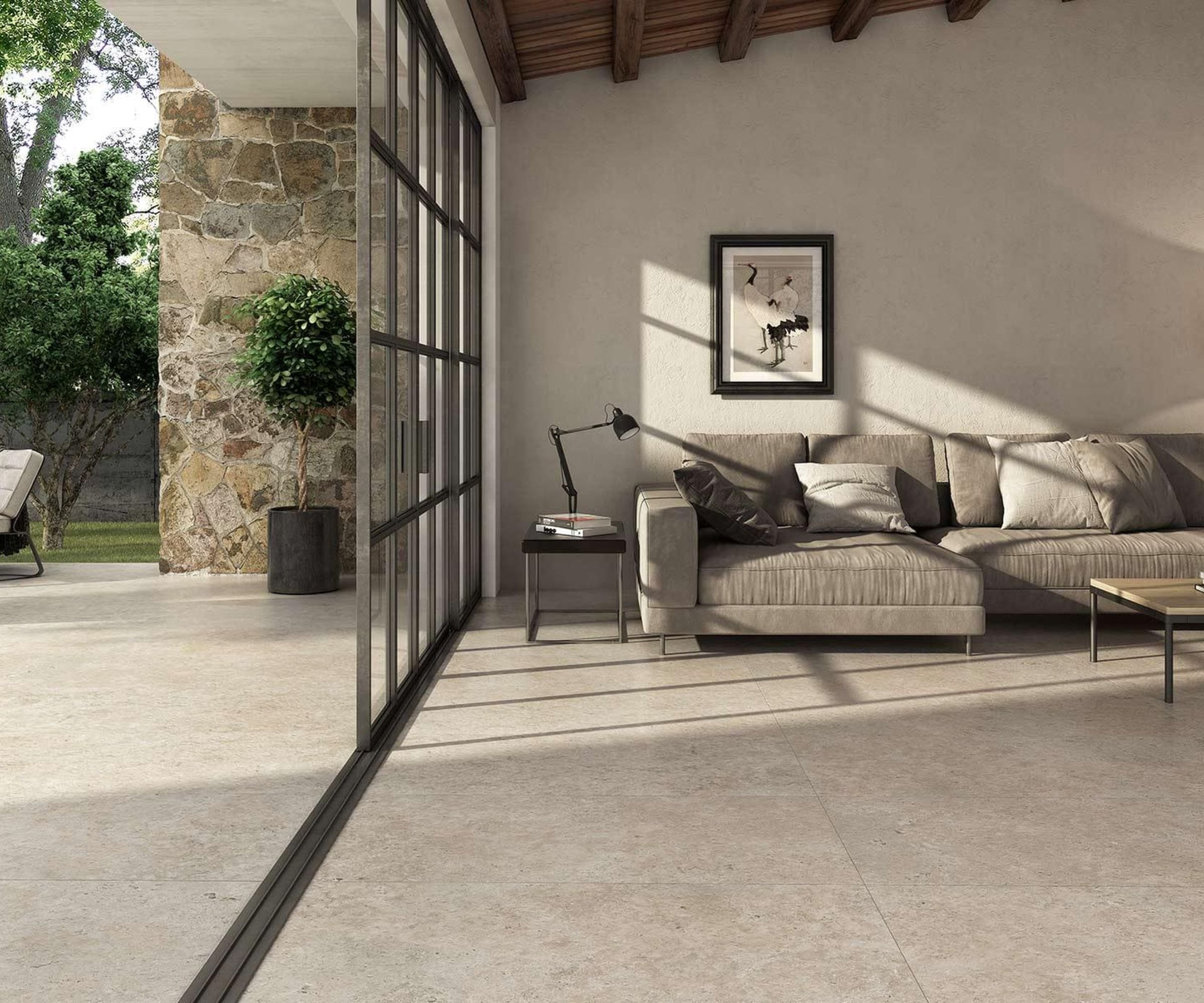 A seamless indoor&ndash;outdoor living space with large-format stone-look tiles running from the sitting room to the patio. Neutral tones, natural light and a modern sectional sofa create a calm, contemporary feel perfect for open-plan homes.