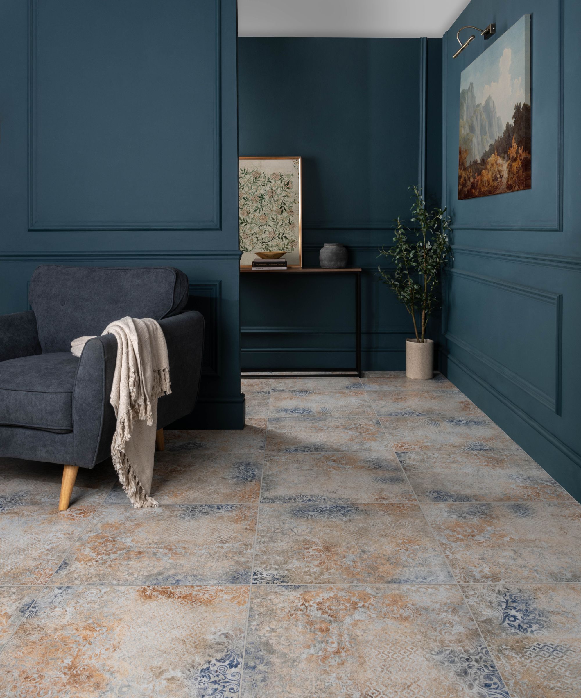 Elegant living room featuring distressed patterned floor tiles, dark blue wall panelling, and a charcoal armchair with a throw.