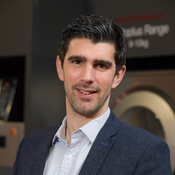 male with short dark hair stood in kitchen wearing navy suit jacket and white shirt