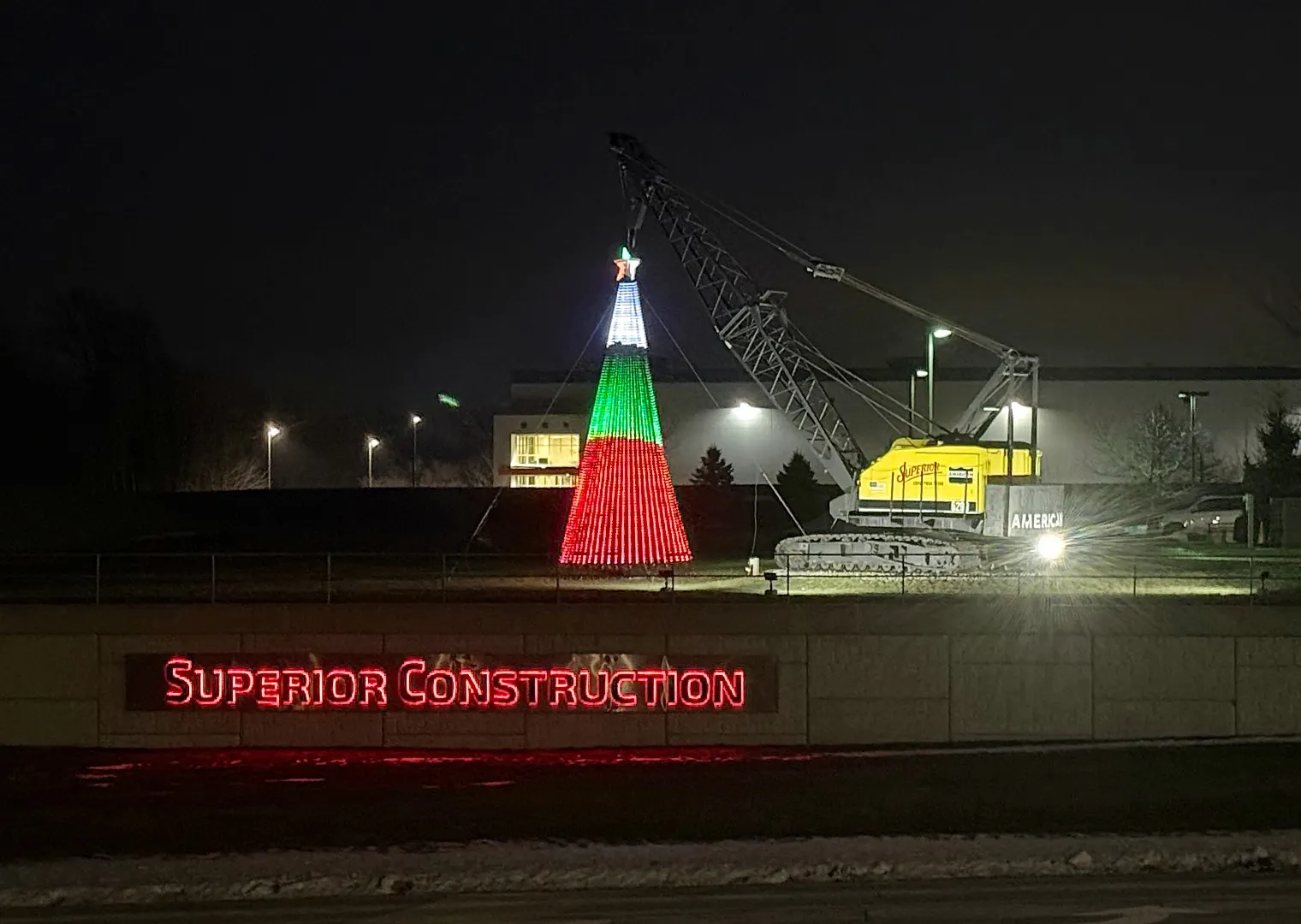 A tall piece of heavy machinery holds up a multicolored metal Christmas tree.