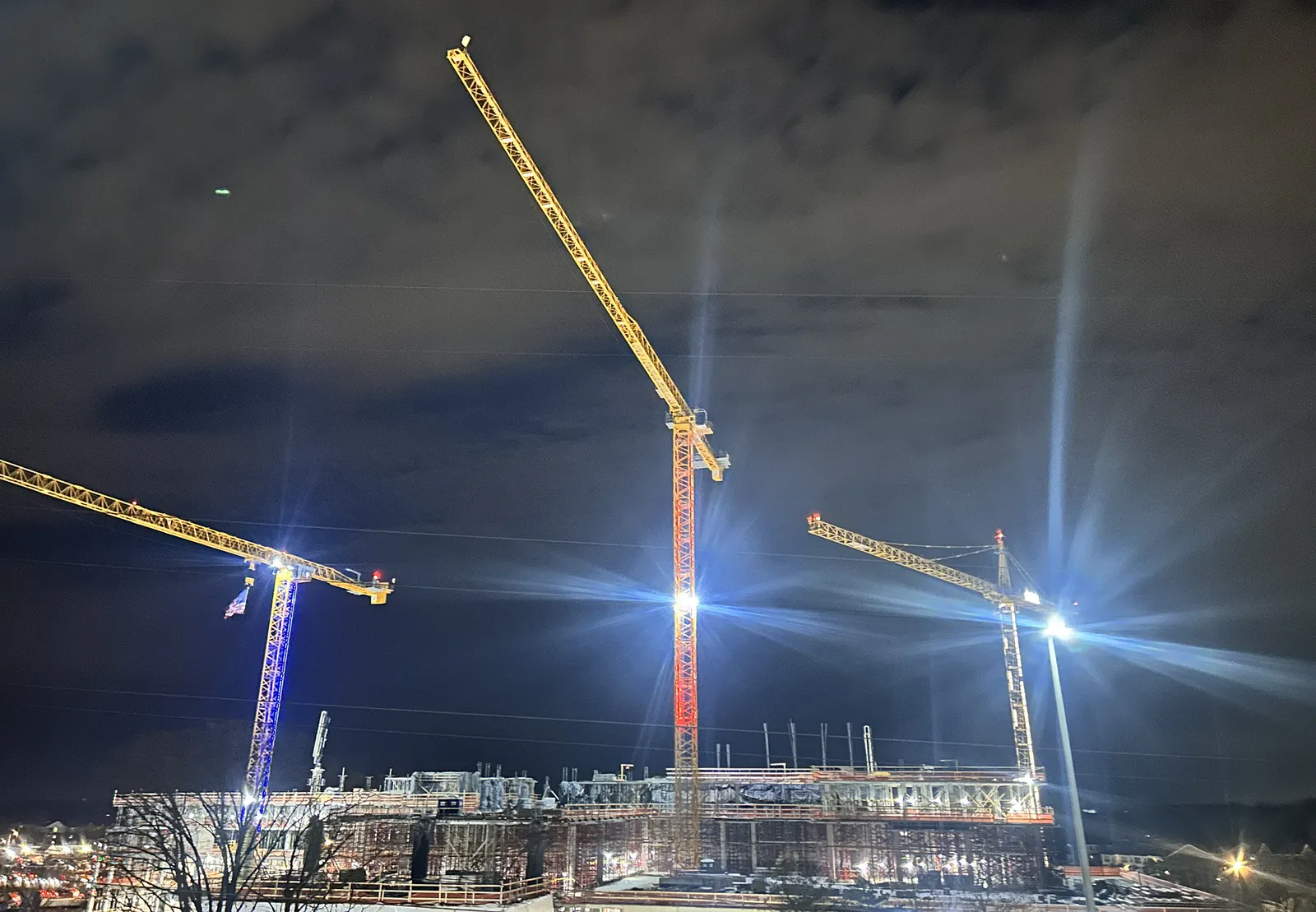 Three cranes rise high in the night sky with lights affixed to their metal.