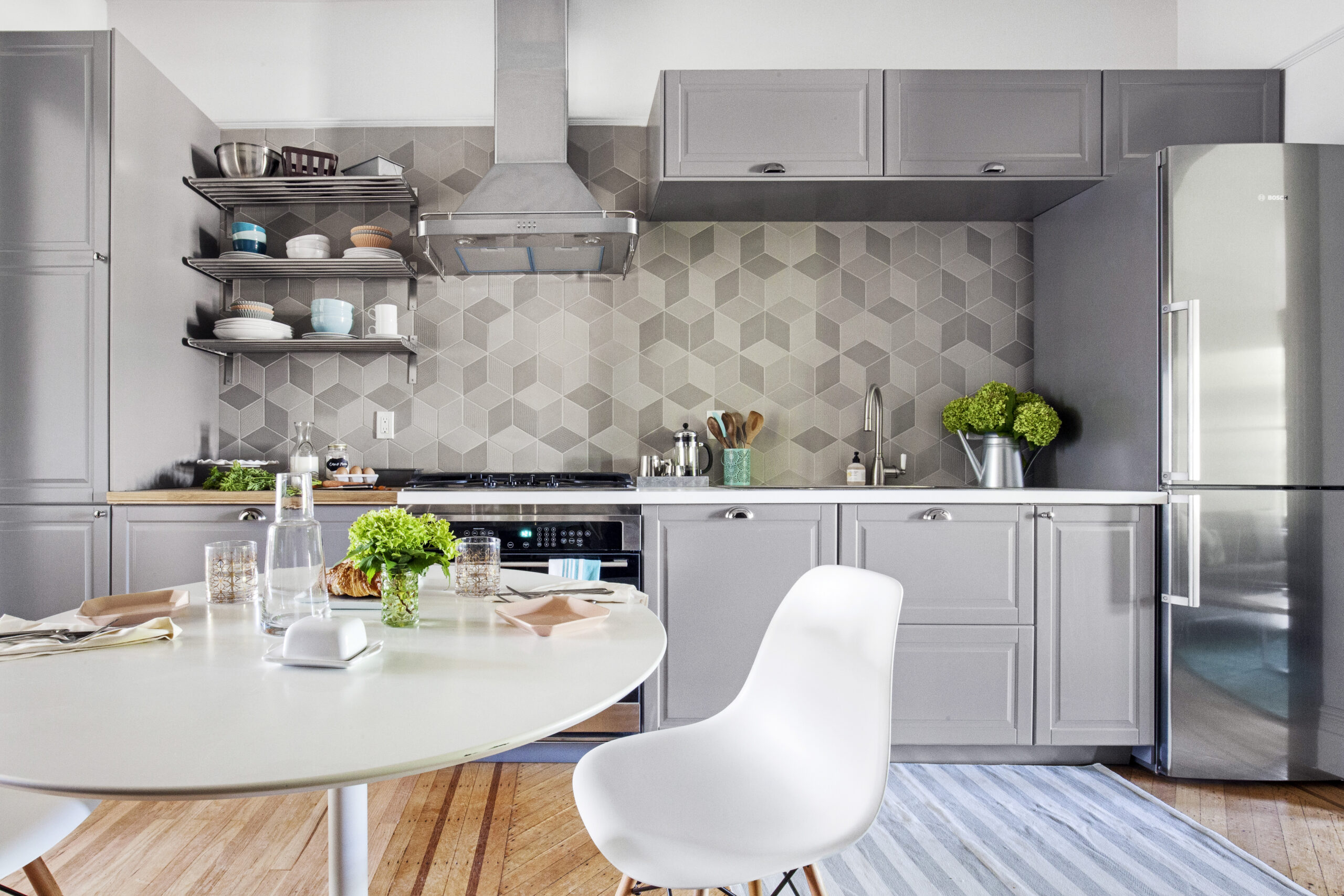 A bright gray kitchen with geometric backsplash, open shelving, and a small dining area styled for everyday use.