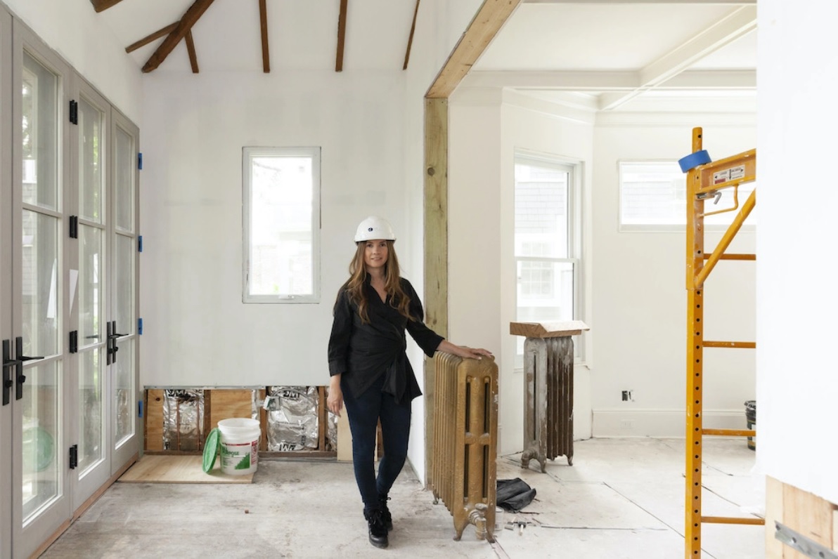 Woman wearing a hard hat standing in an interior of a home being remodeled.