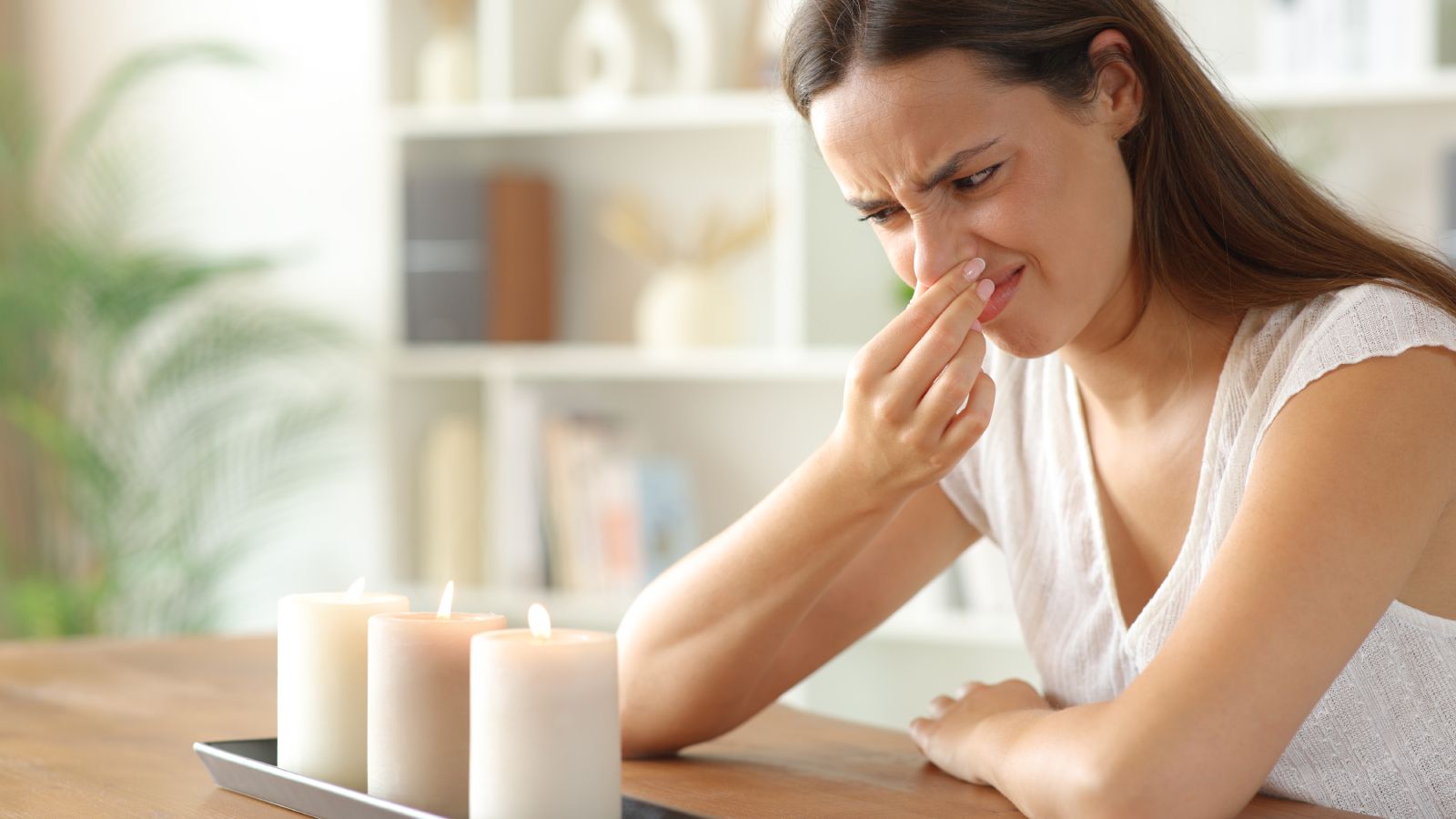 female holding nose sat at table looking at candles