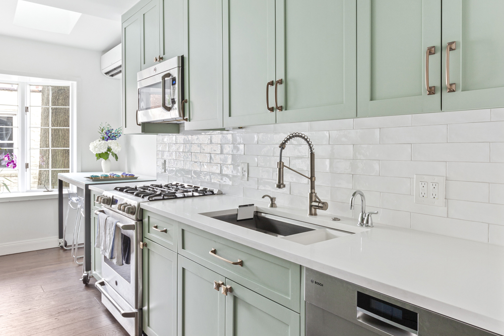 Kitchen with sage green Shaker cabinetry, brass handles, and white subway backsplash design