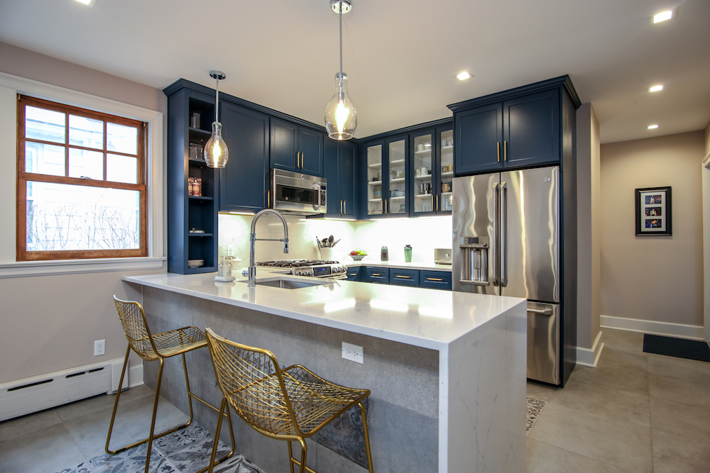 Kitchen with deep blue Shaker cabinet doors, quartz peninsula, and slab flooring
