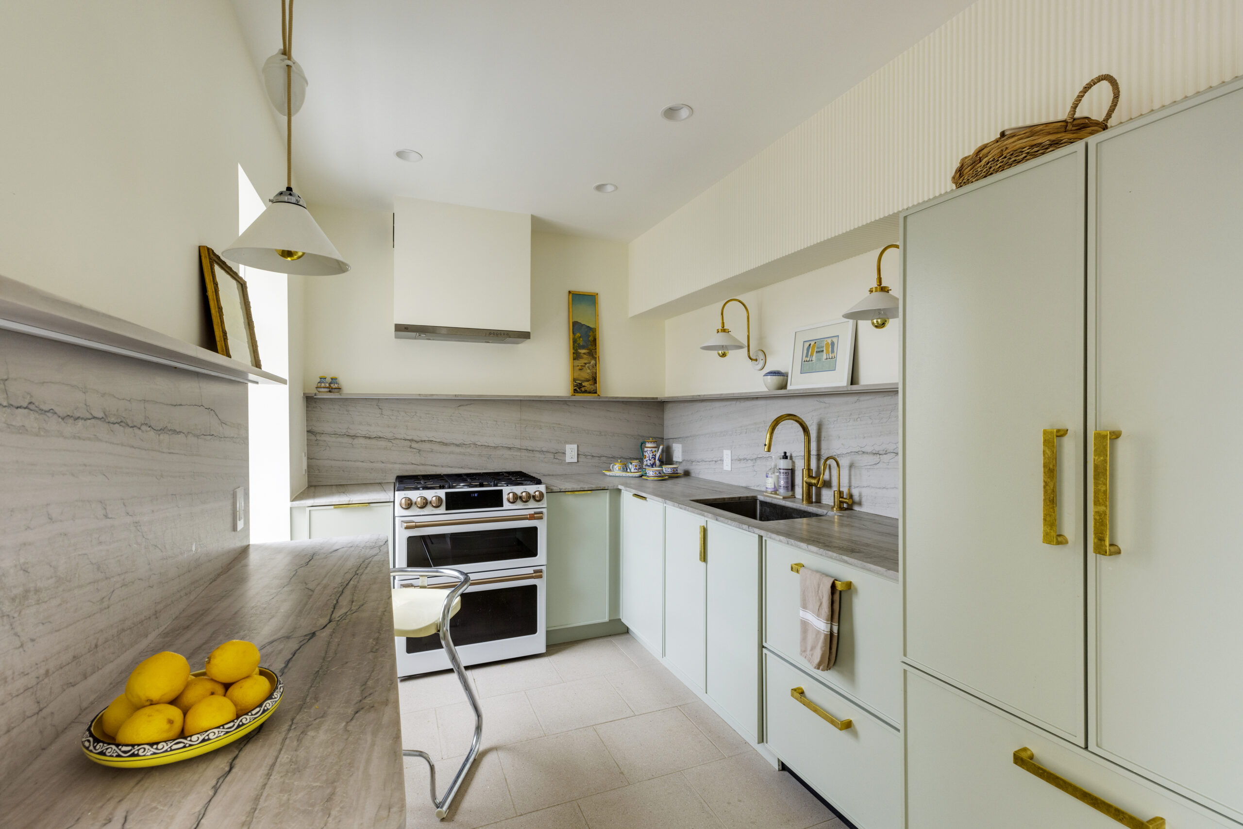 Kitchen with natural slab backsplash, light green slim Shaker cabinets, and golden fixtures